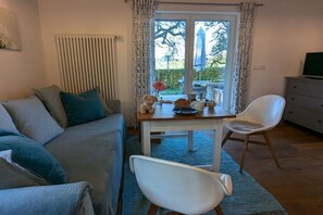A cozy living room with a sofa, a dining table with chairs, a radiator, and a television on a dresser. - Michaela holiday apartment (Heiligenberg)