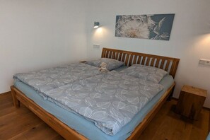 A bedroom with a wooden bed, a small bedside table, a wall-mounted light, and a floral painting. - Michaela holiday apartment (Heiligenberg)