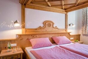 Ein Hotelzimmer mit einem hölzernen Kopfteil, zwei Betten mit Karomuster-Bettwäsche, Nachttischen mit Lampen und einem Fenster mit Vorhängen.