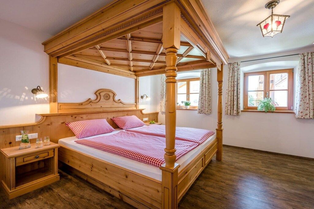 Ein hölzernes Himmelbett mit Kopfteil, ein Nachttisch und ein Fenster mit Vorhängen.