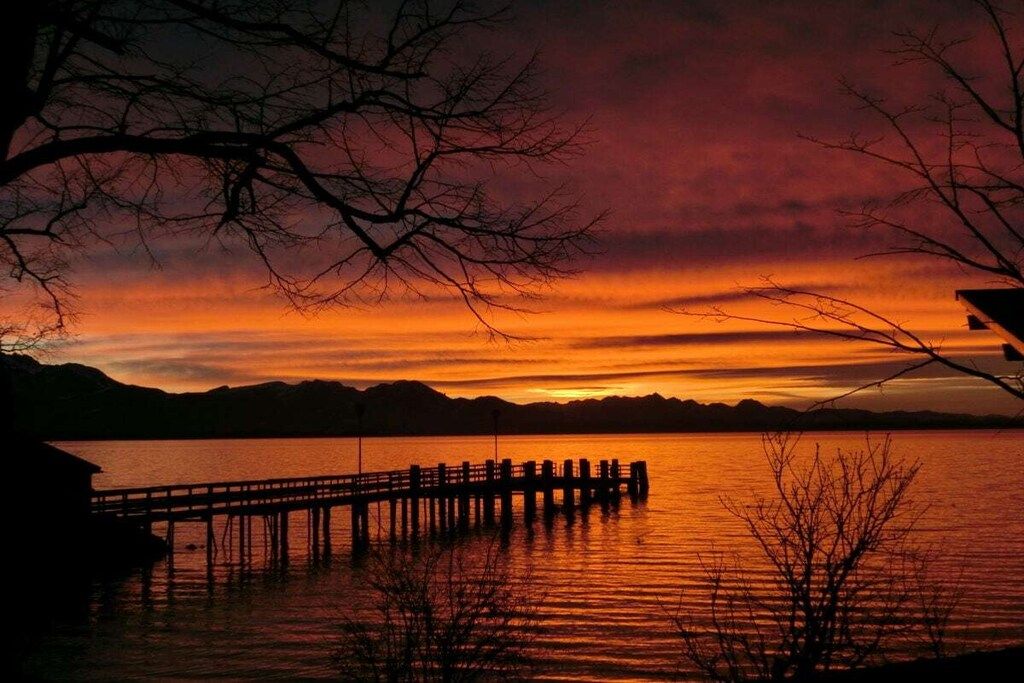 Een zonsondergang boven het water, met een steiger die erin uitkomt.