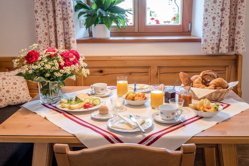 A breakfast table set with plates of food, glasses of juice, and a vase of flowers.