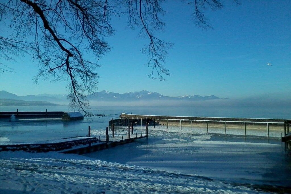 Un lac gelé avec une jetée qui s’avance sur l’eau, entouré de montagnes en arrière-plan.