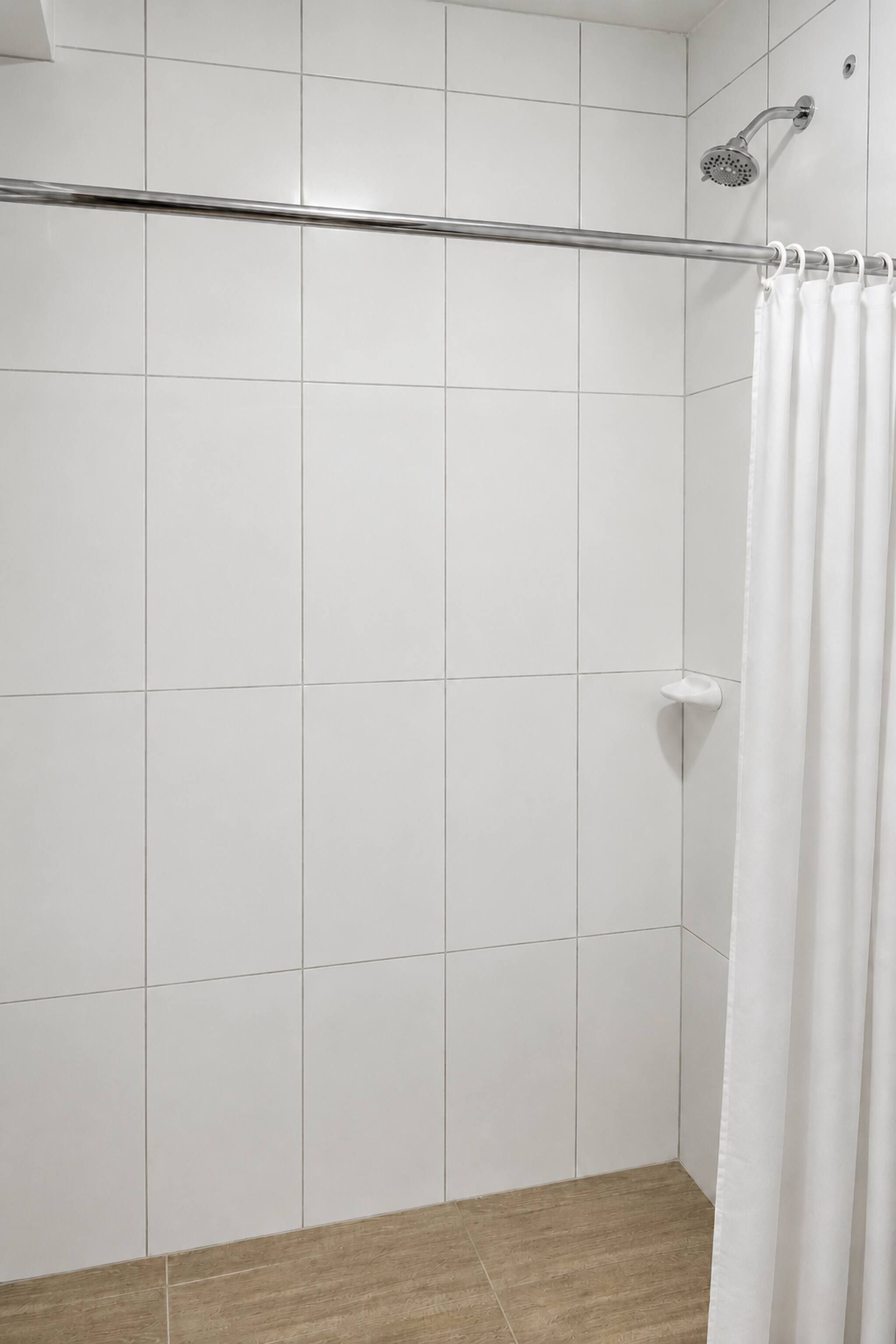 A shower area with white tiles, a showerhead, and a white curtain.
