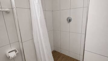 A shower area with a white shower curtain, a handheld showerhead, and a wall-mounted faucet.