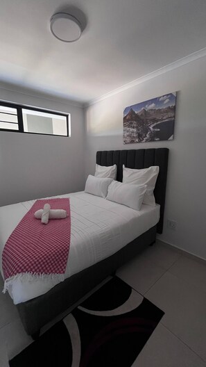 Un dormitorio moderno con una cama, una ventana, un cuadro en la pared y una lámpara de techo.