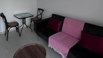 A modern living room with a black sofa, a round wooden coffee table, a small square table, two chairs, and a wall-mounted abstract painting.