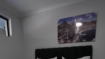 A hotel room with a bed, a red and white checkered blanket, white pillows, and a framed picture of a mountain landscape on the wall.