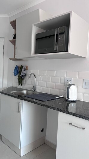 A modern kitchen with white cabinetry, a stainless steel sink, and a microwave. - Tranquil 1-Bedroom Apartment in Roodepoort, South Africa (Roodepoort)