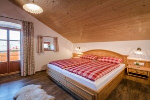 Ein Schlafzimmer mit Holzboden, einem großen Bett mit karierter Bettwäsche, einem Nachttisch und einem Fenster mit Vorhängen.