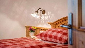 Ein Schlafzimmer mit kariertem Bettbezug, einem Nachttisch mit Blumenvase und einer Wandleuchte.