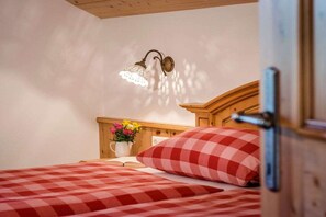 A bedroom with a checkered bedspread, a bedside table with a vase of flowers, and a wall-mounted light fixture. - Oven bench directly on Lake Chiemsee (Chieming)