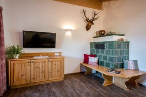 A living room with a wooden cabinet, a mounted television, a bench with cushions, and a decorative deer head on the wall. - Oven bench directly on Lake Chiemsee (Chieming)