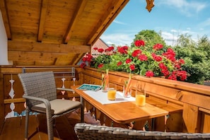An outdoor wooden deck with a table and chairs, surrounded by red flowers and greenery. - Oven bench directly on Lake Chiemsee (Chieming)