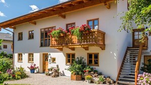 Ein traditionelles Chalet mit Balkon, der mit Blumen geschmückt ist, einer Holztreppe und einer Schotterauffahrt.