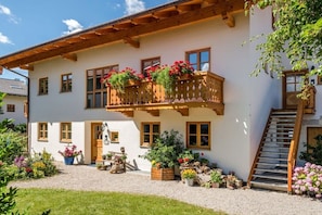 A traditional chalet with a balcony adorned with flowers, a wooden staircase, and a gravel driveway. - Oven bench directly on Lake Chiemsee (Chieming)