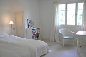 A white room with a bed, a chair, a small table, a bookshelf, and a window with curtains. - 2 Alpenblick - Steineckhof (Schopfheim)