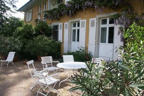 A building with a garden patio featuring white metal chairs and a table, surrounded by lush greenery and purple flowering vines. - 2 Alpenblick - Steineckhof (Schopfheim)