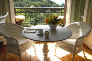 A balcony with wicker chairs, a round table, a vase with flowers, and a view of a green landscape. - 2 Alpenblick - Steineckhof (Schopfheim)