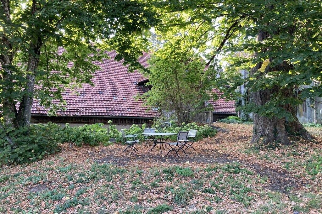Punatiilikattoinen rakennus, jonka ympärillä on puita ja jossa on nurmikkoalue sekä pöytä ja tuoleja.