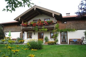 A traditional chalet with a balcony adorned with flowers, a wooden deck, and a garden with various plants and flowers. - 2 "Beim Paulfischer" directly on Lake Chiemsee (Chieming)