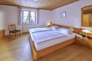 Una cama con estructura de madera, dos almohadas y una mesita de noche con una lámpara y un plato de manzanas.