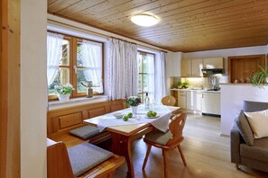 A cozy dining area with a wooden table, chairs, and a bench. There is a kitchen in the background with cabinets and a countertop. - 2 "Beim Paulfischer" directly on Lake Chiemsee (Chieming)