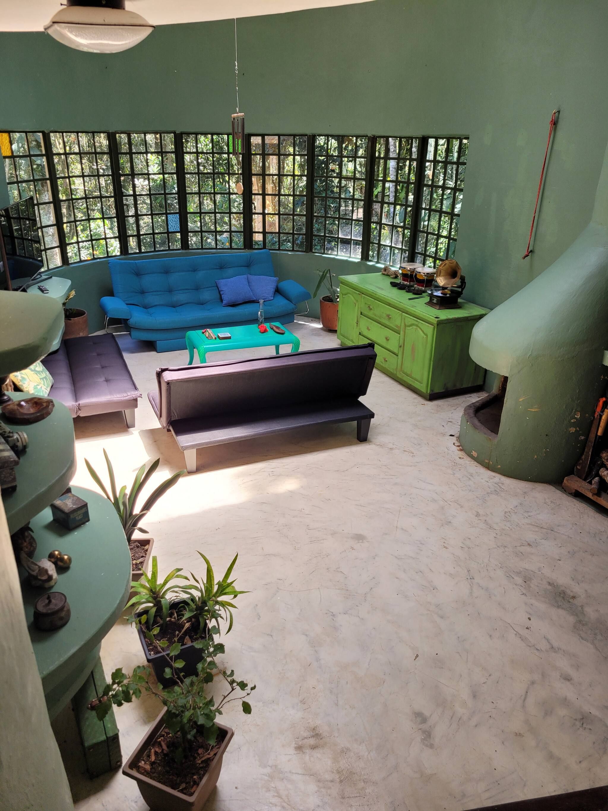 A room with a blue sofa, a green cabinet, and a window with a view of trees.