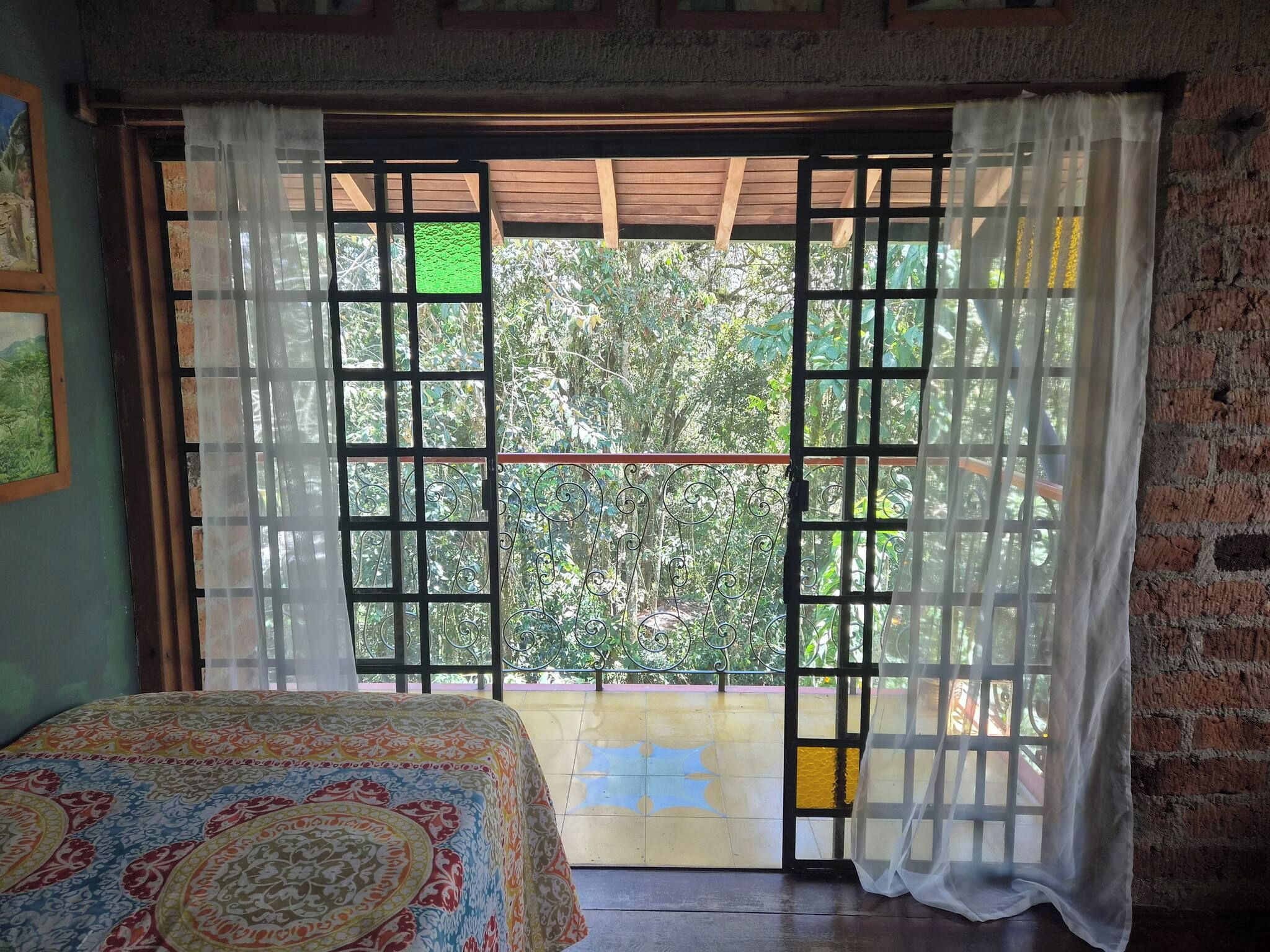 Ein Zimmer mit einem Bett, einem Fenster mit Blick auf Grünflächen und einer Ziegelwand.