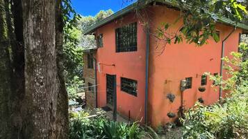 A building with a red exterior, surrounded by dense foliage and a large tree.