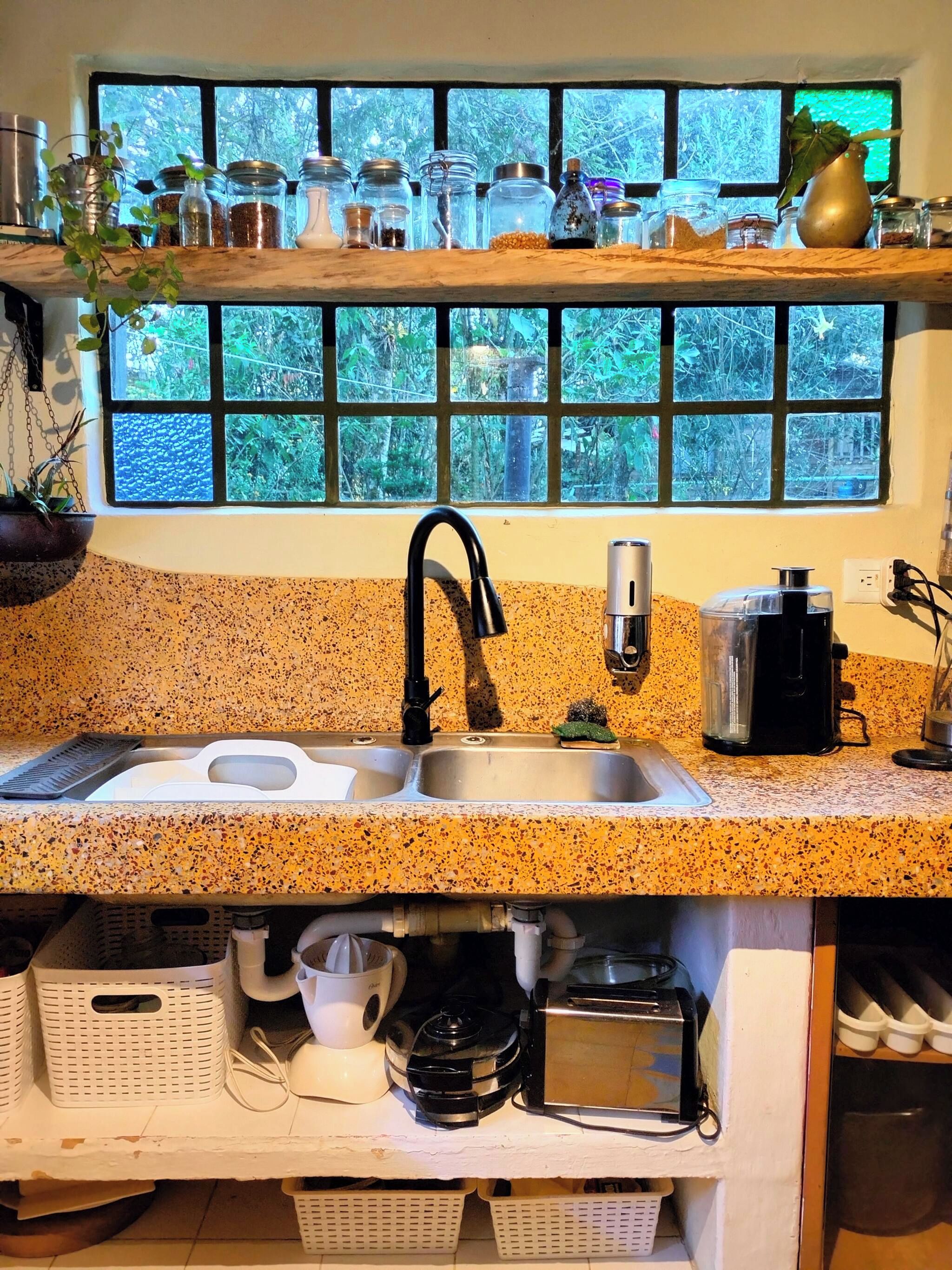 Eine Küche mit einer Granit-Arbeitsplatte, einem schwarzen Wasserhahn, einer Kaffeemaschine und einem Fenster mit Blick auf Grünflächen.
