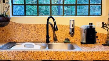 Eine Küche mit einer Granit-Arbeitsplatte, einem schwarzen Wasserhahn, einer Kaffeemaschine und einem Fenster mit Blick auf Grünflächen.