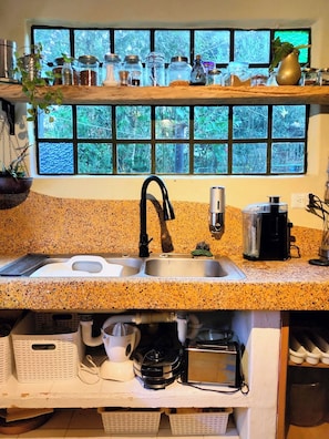 Eine Küche mit einer Granit-Arbeitsplatte, einem schwarzen Wasserhahn, einer Kaffeemaschine und einem Fenster mit Blick auf Grünflächen.