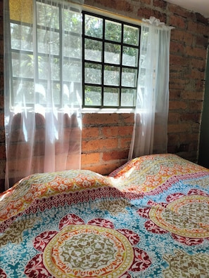 Ein Zimmer mit einer Ziegelwand, einem Fenster mit Gittermuster und einem Bett mit gemustertem Überwurf.