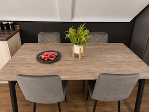 Een eettafel met een bord lekkernijen, een potplant en een klein kastje met bakjes.