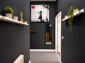 Un pasillo con una obra de arte blanco y negro, un espejo, una planta y una estantería con objetos decorativos.