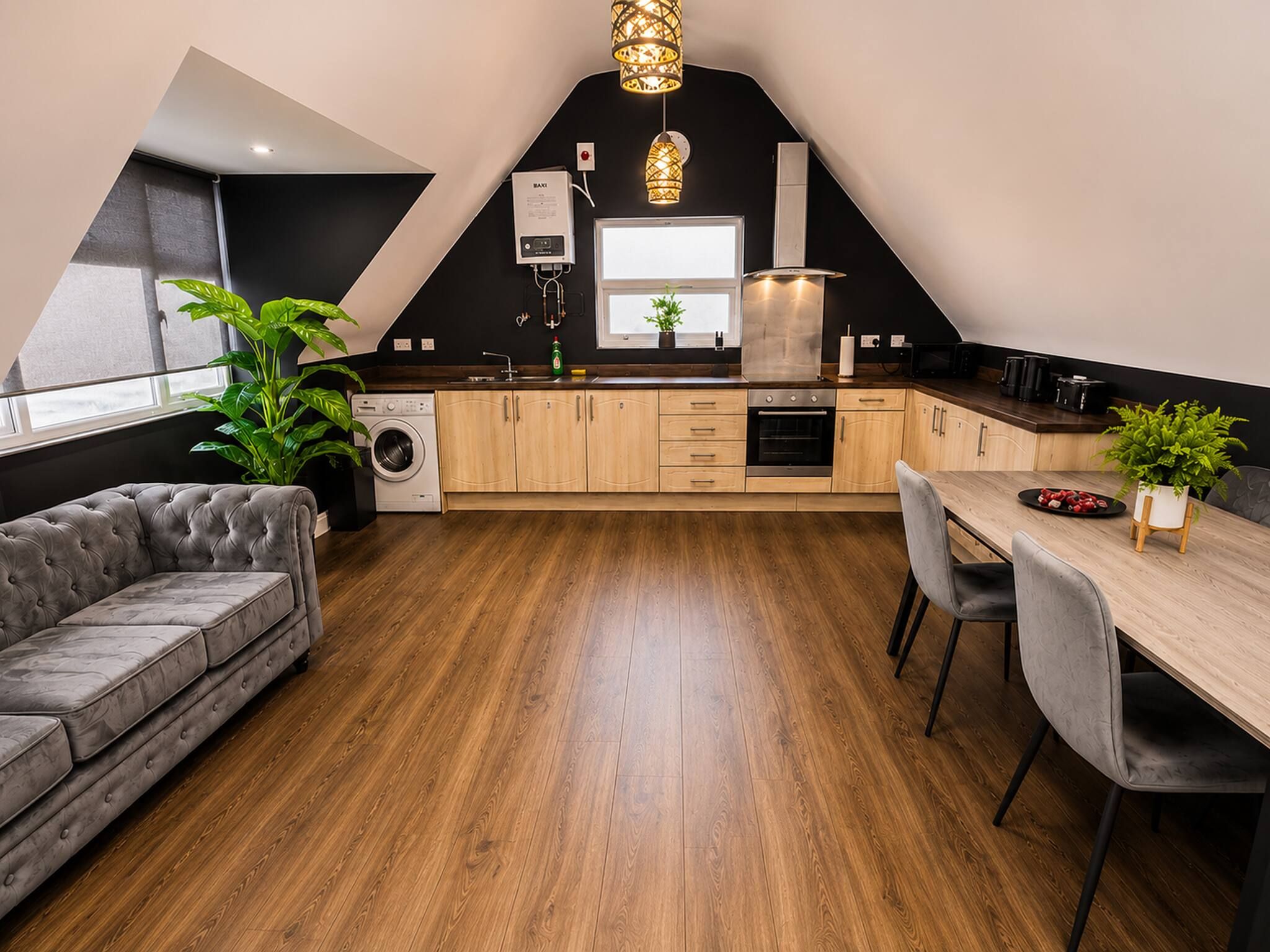 Una cocina moderna con comedor, piso de madera y sofá gris.