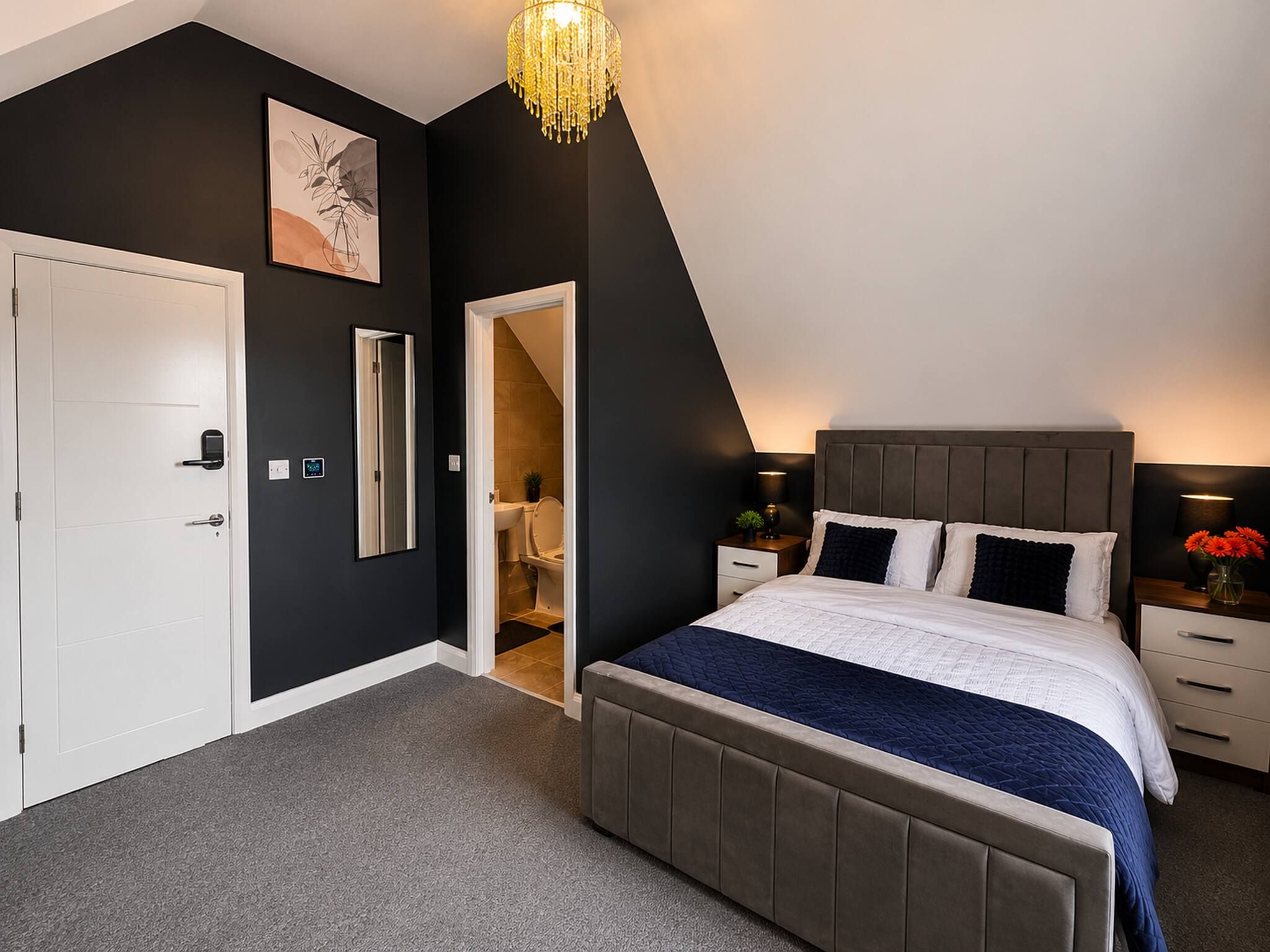 A bedroom with a bed, bedside tables, a nightstand, a chandelier, a door, and a mirror.