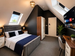 Een moderne slaapkamer met dakraam, een bed met een gewatteerde deken, een bureau met een computer en een televisie waarop streamingdiensten worden afgespeeld.