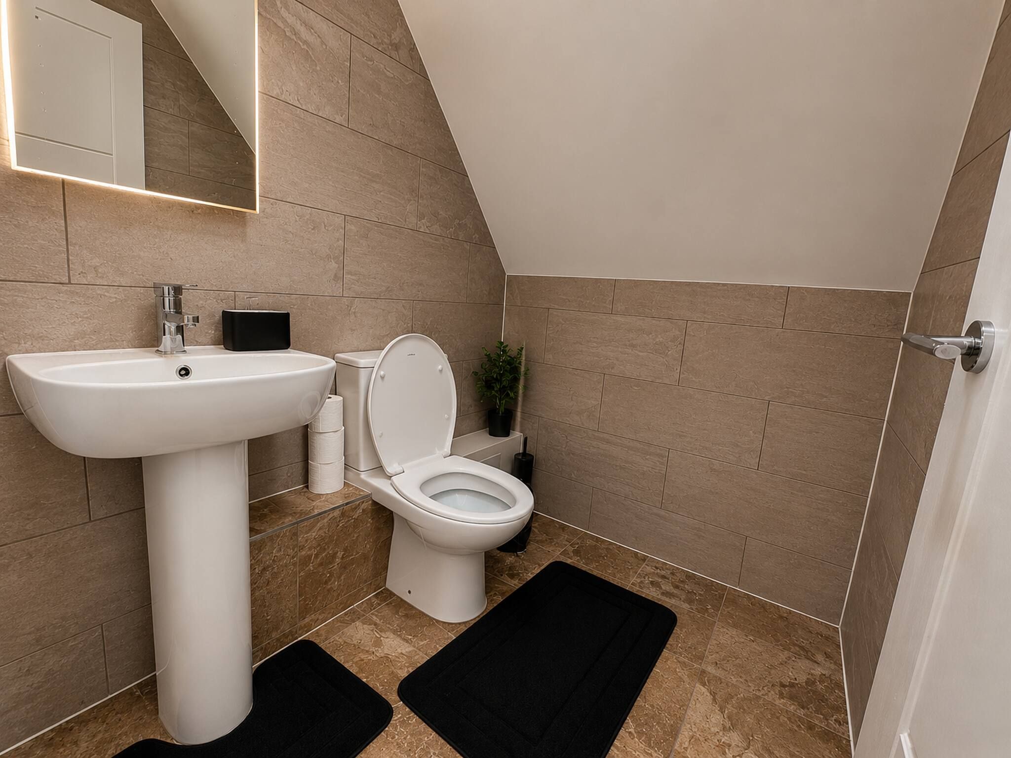 A modern bathroom with a white pedestal sink, a toilet, and a mirror above the sink.