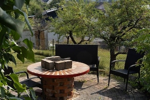 Uma área de estar ao ar livre circular, com mesa e cadeiras de tijolo, cercada por vegetação e um muro.