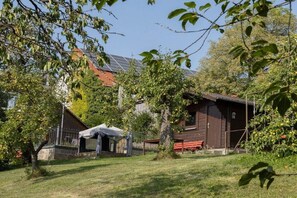Una casa de madera rústica con techo inclinado, rodeada de árboles y un patio cubierto de césped.