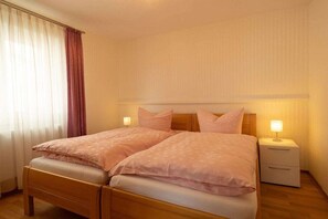 Una cama doble con estructura de madera, dos mesitas de noche con lámparas y un ventanal con cortinas.