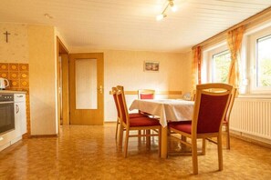 Un comedor con mesa y sillas, una cocina con horno, y un ventanal con cortinas.
