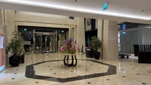 Eine Hotelhalle mit einem runden Tisch in der Mitte, Blumentöpfen und einem Glastürbereich.
