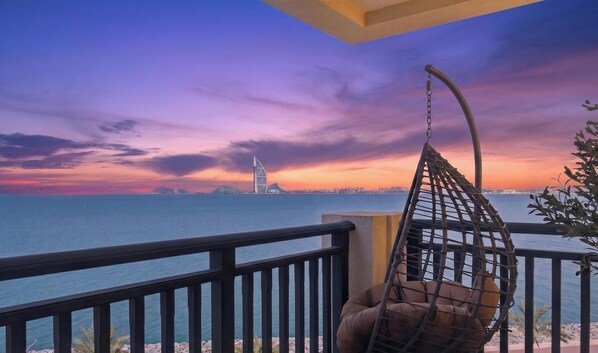 A balcony with a view of a city skyline at sunset, a hanging chair, and a railing. - Full Burj View Private Sauna & Beach (Dubai)