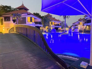 A wooden bridge leading to a swimming pool area with multiple buildings in the background. - Full Burj View Private Sauna & Beach (Dubai)