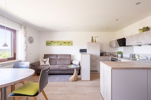 A modern kitchen with white cabinets, a dining area with a round table and chairs, and a gray sofa with a decorative pillow. - Holiday apartment in Kappelrodeck with Wi-Fi (Kappelrodeck)