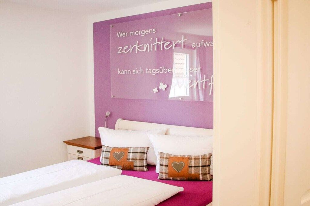 Une chambre à coucher avec un lit, deux oreillers, une table de chevet et un mur sur lequel est écrit un message en allemand.