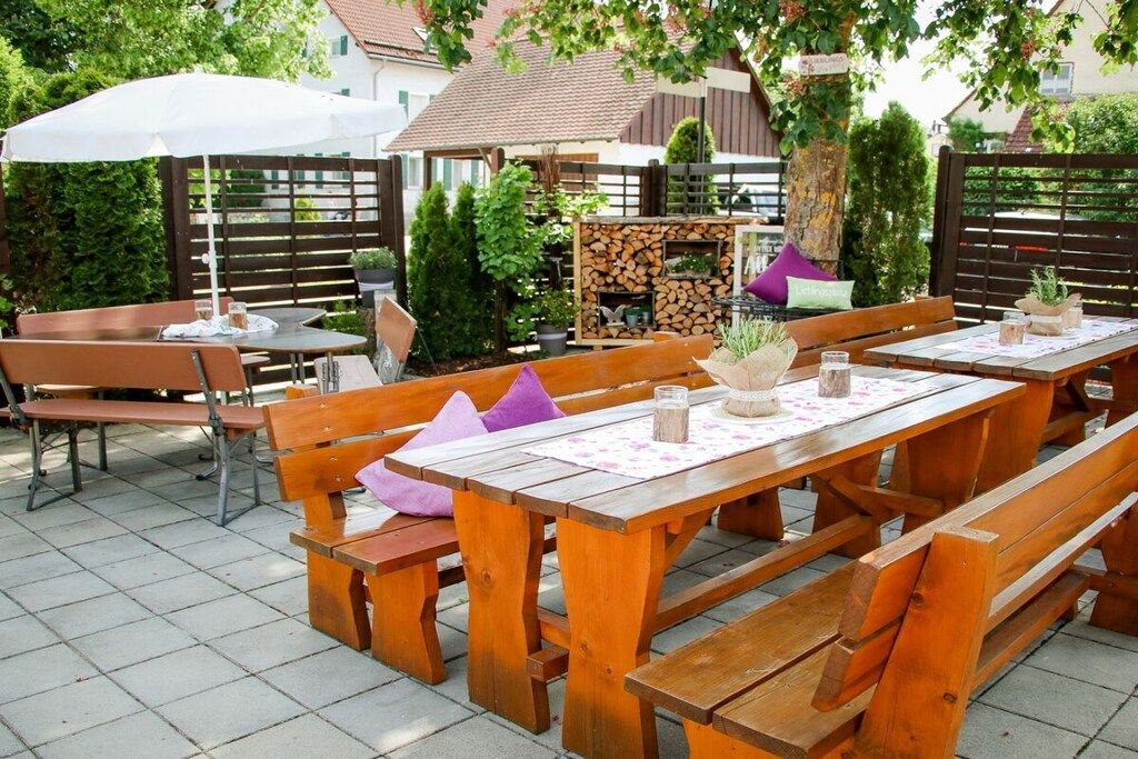 Eine Terrasse im Freien mit Holztischen und -bänken, umgeben von viel Grün und einem Zaun.